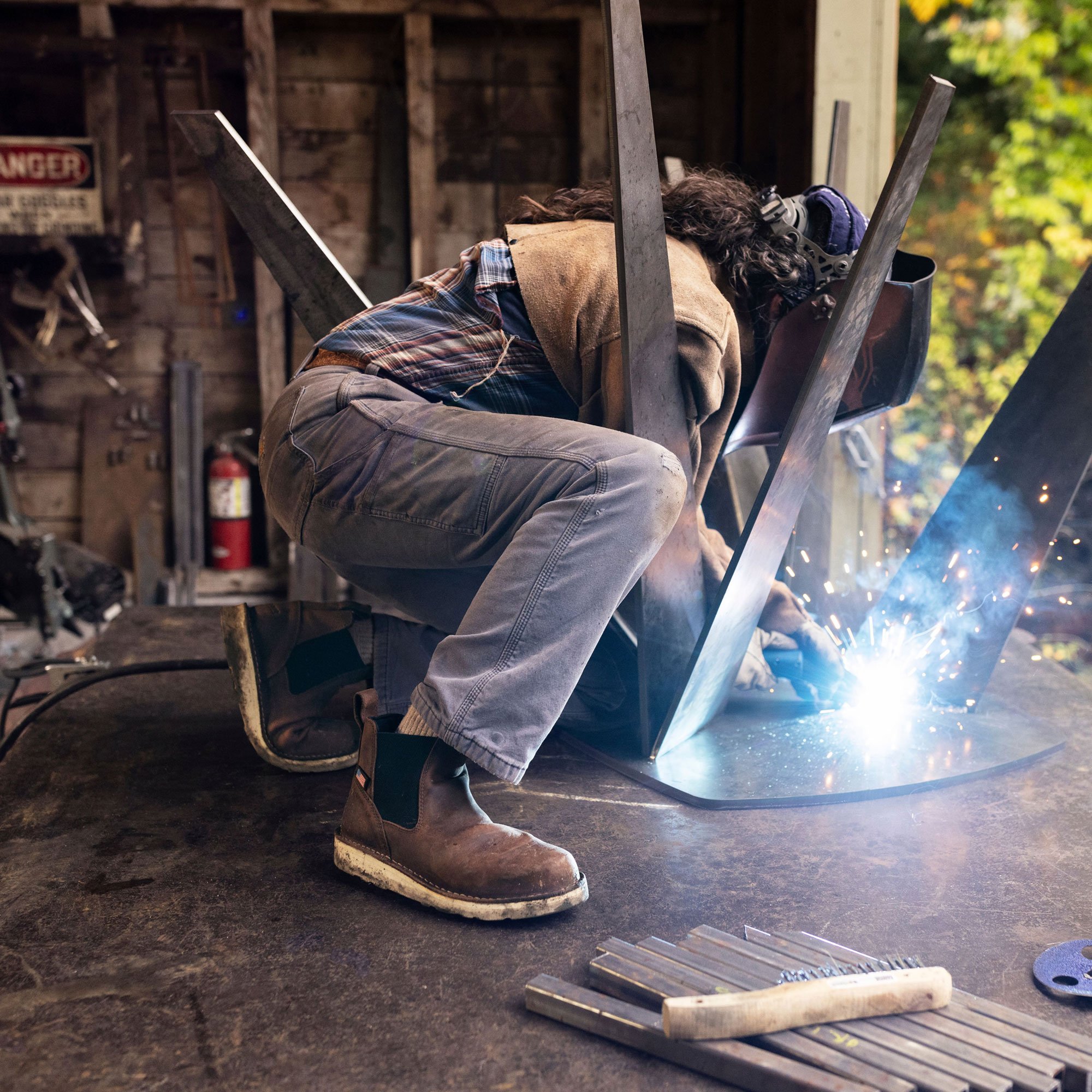 A woman stands on a rock with her hands in her yellow jacket wearing black leggings and brown leather boots with a sharp rock face in the background.