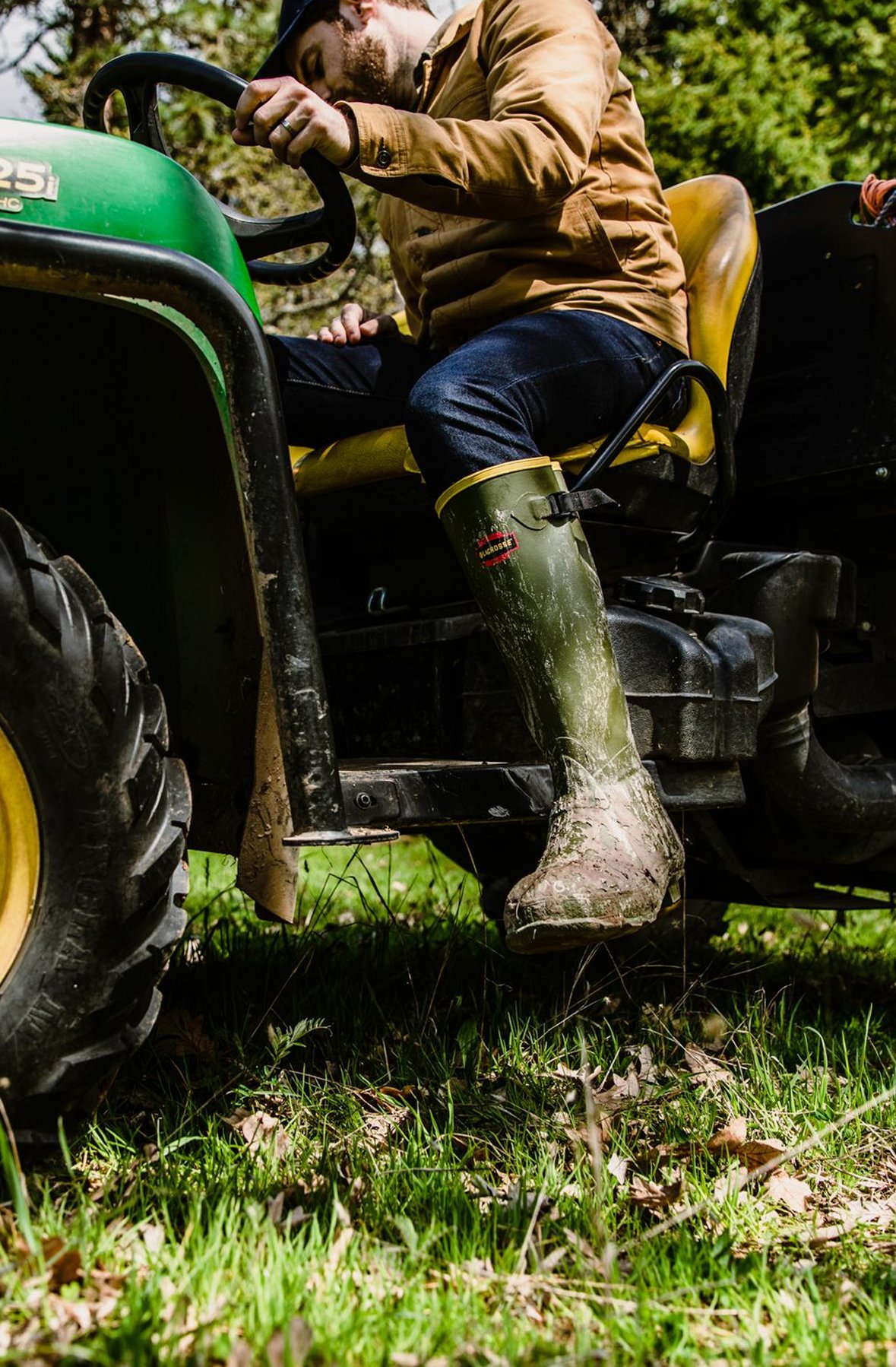 A man in green rubber boots on a John Deere tractor